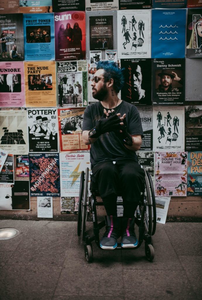 An image of Kris in his wheelchair, wearing his futuristic MiMu Gloves
